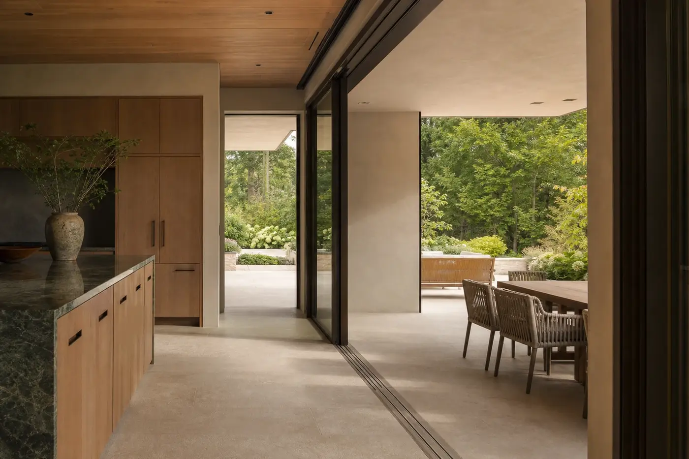 Nearly flush stone threshold beneath open bronze-framed glass doors between a kitchen and covered terrace