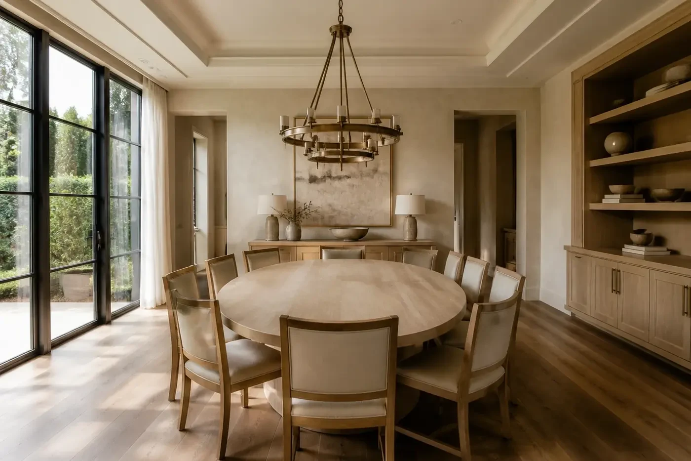New luxury custom-home dining room with an oval white oak table, coordinated chandelier, tray ceiling, windows, and built-in storage