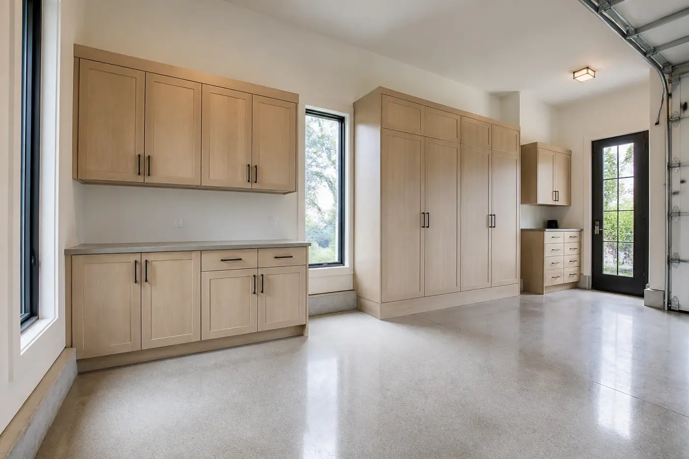 New luxury custom-home garage with coordinated white-oak cabinets, a landing counter, tall storage, and natural daylight