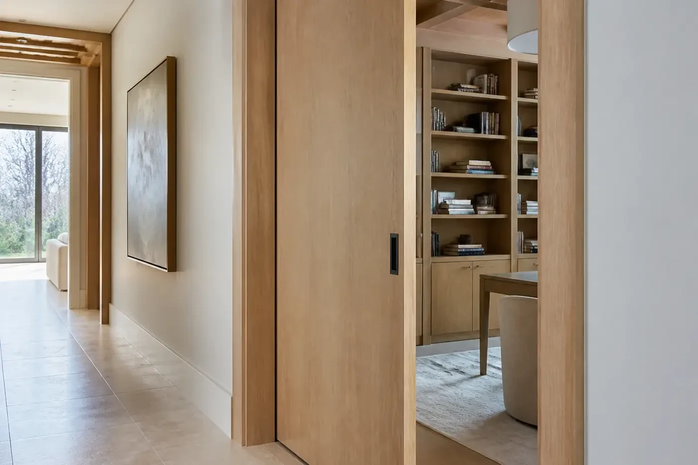 Tall white-oak pocket door connecting a new custom-home library and residential gallery