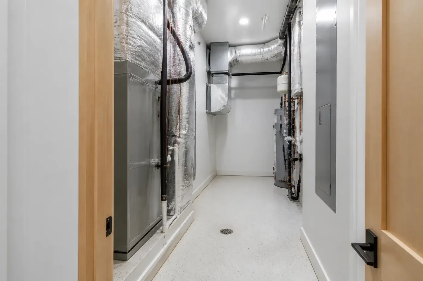 New custom-home mechanical room viewed through a broad residential service doorway with a clear equipment replacement path