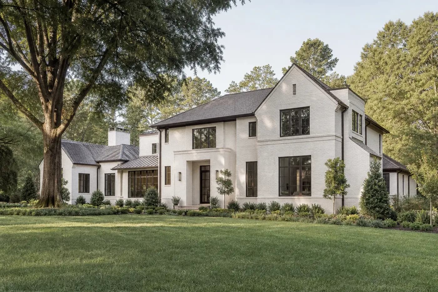 Refined Charlotte custom home with coherent rooflines, limewashed brick, bronze windows, and mature landscaping