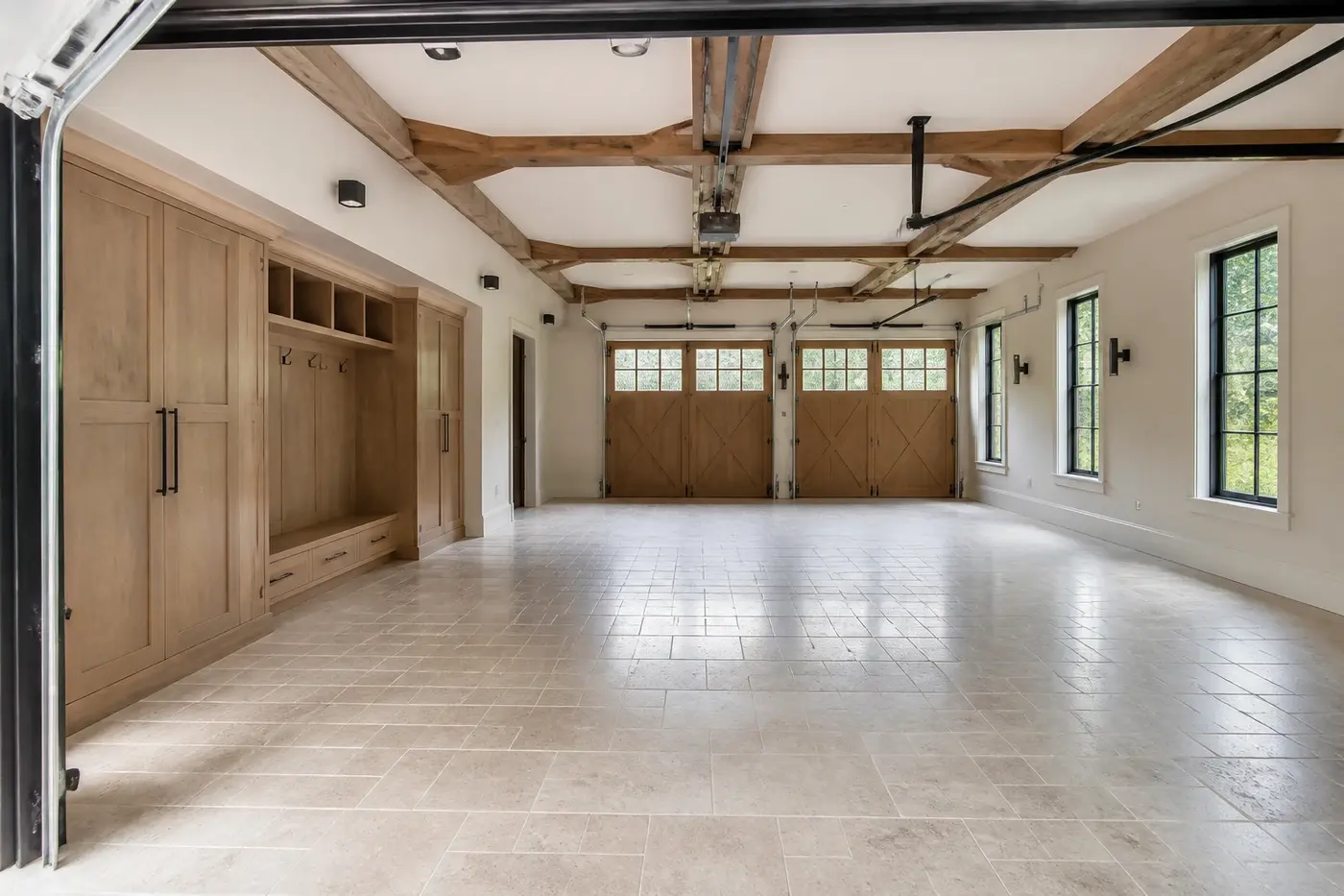 New Charlotte luxury custom-home garage with carriage-style doors, white-oak storage, tall windows, and a clear open floor